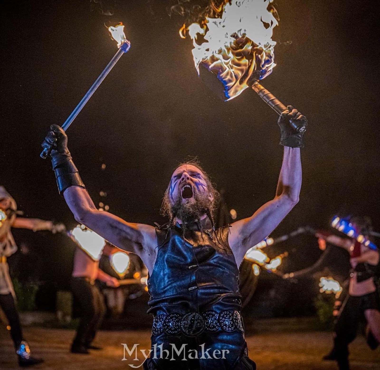 A fire dancer roars with a flaming club in each hand
