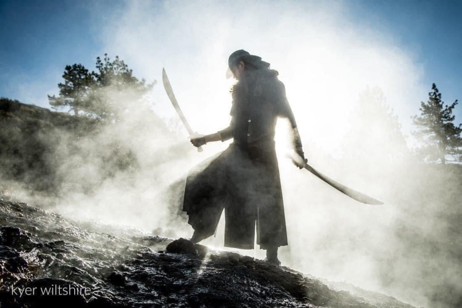 A swordsman turns through the mist with twin blades drawn