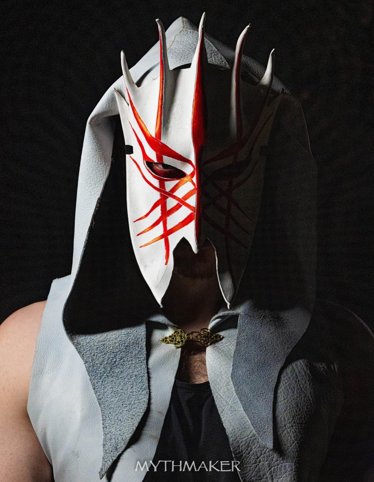 A white leather mask streaked with red beneath a pale hood