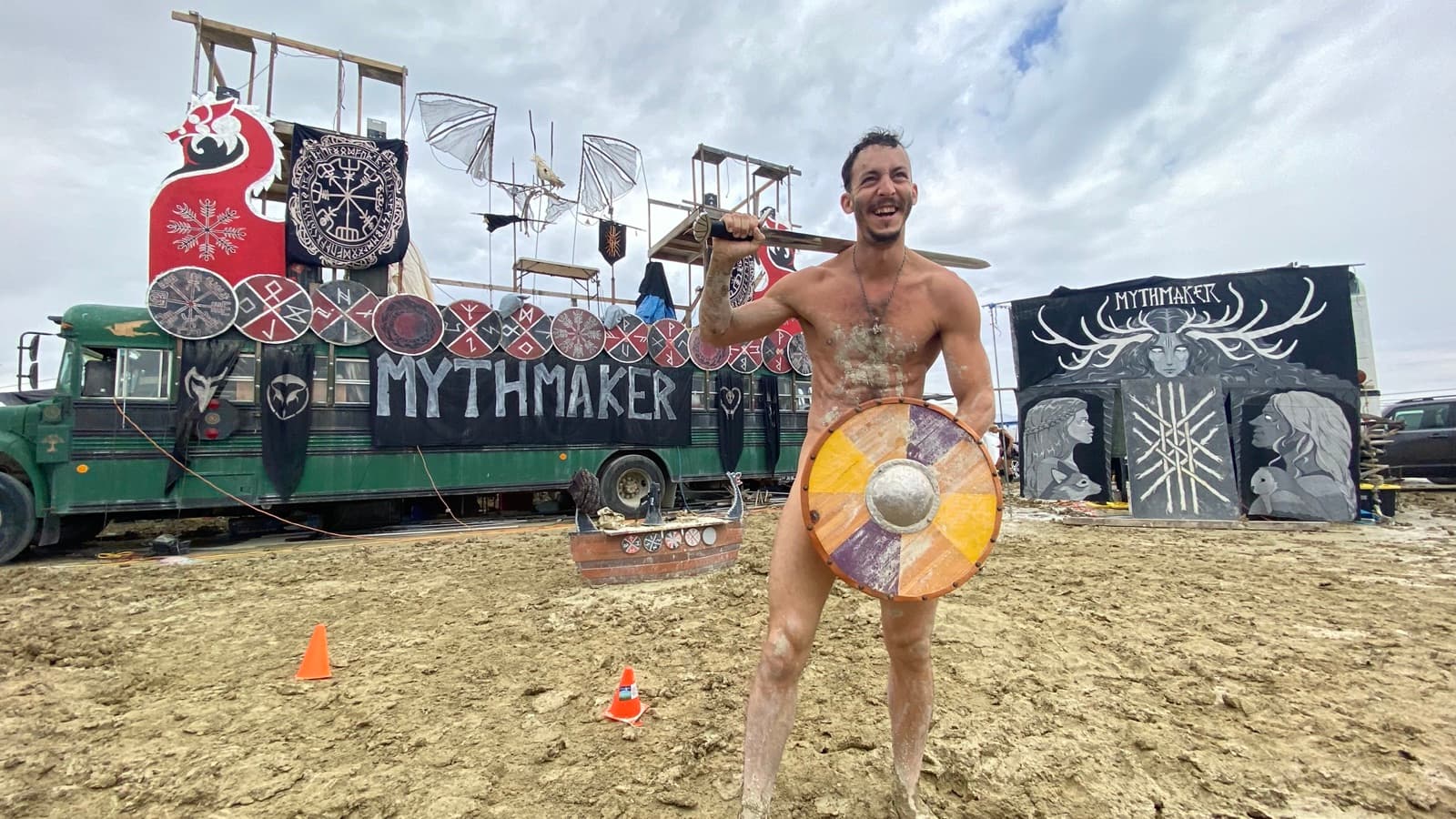 A mud-caked reveller with sword and shield before the MythMaker bus